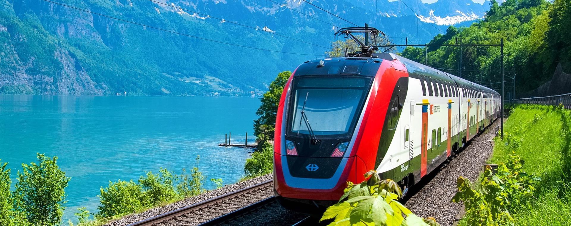 Train électrique qui passe tout près d'un lac et des montagnes