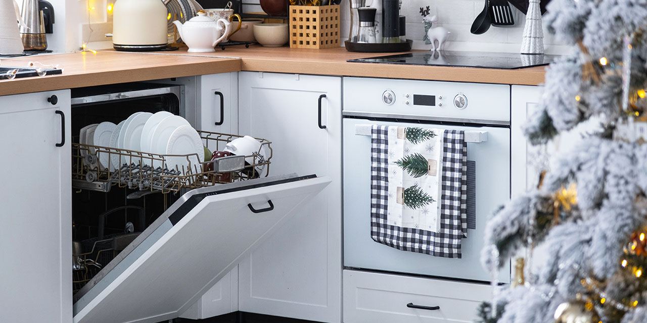 Holiday kitchen with an open dishwasher full of clean dishes, a decorated oven, and a lit Christmas tree