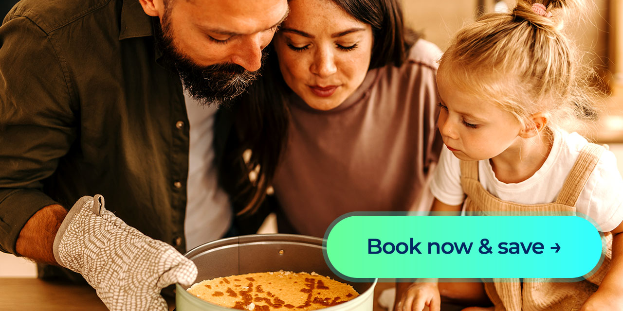 Family leaning over a kitchen counter as a parent carefully lifts a freshly baked cake from the oven while a young child watches closely