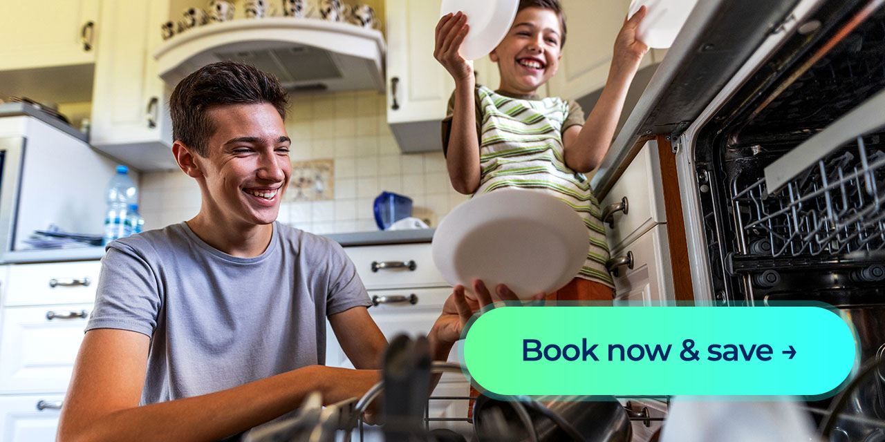 Two kids smile as they load plates into an open dishwasher in a bright kitchen. Button: Book now & save