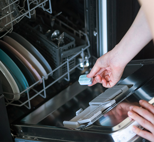 Hand placing a dishwasher detergent pod into the open dispenser inside a dishwasher