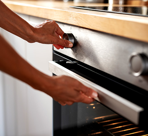 Close-up of someone turning the knob and opening a stainless steel oven door in a kitchen
