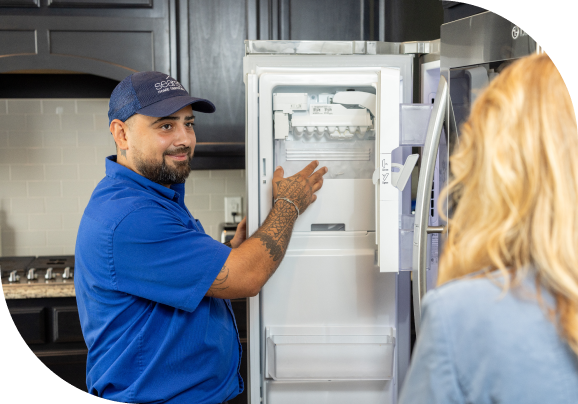 A technician showing a customer an issue with the ice maker in a fridge