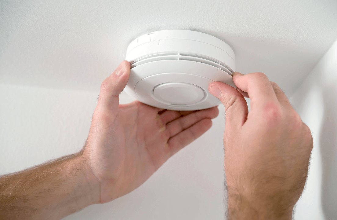 A person resetting a ceiling smoke detector