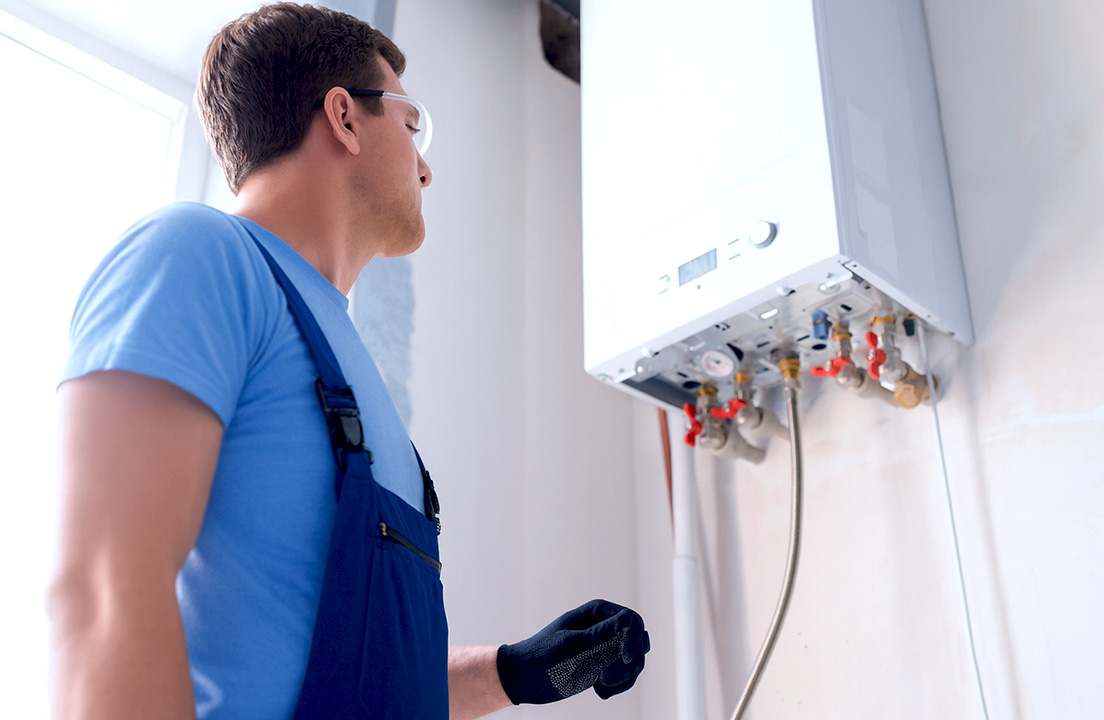 Technician in blue overalls inspecting a modern wall-mounted boiler in a bright utility room