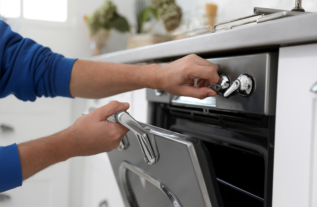 Close-up of a person adjusting the control knob while opening a modern oven in a bright kitchen