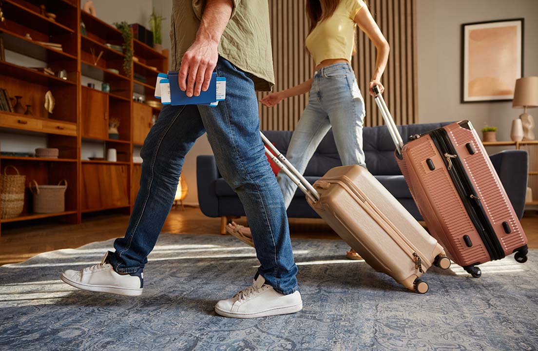 Couple walking through their living room with rolling suitcases and boarding passes, getting ready to travel