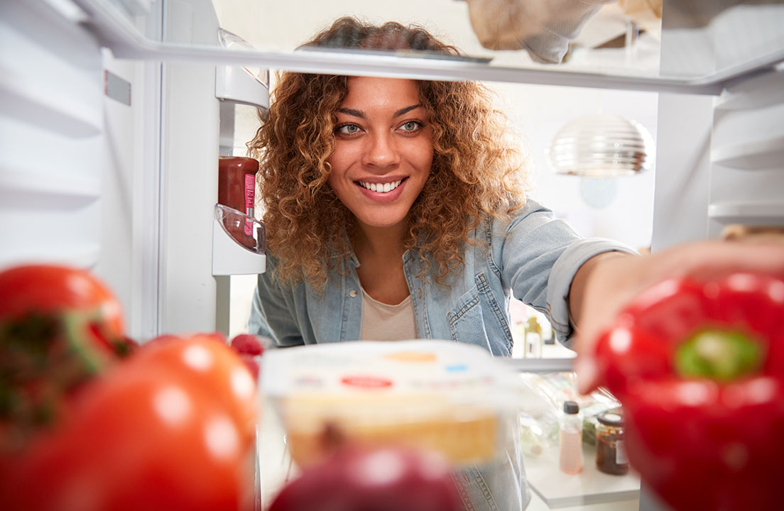 View from inside a refrigerator as a woman reaches in to grab fresh food