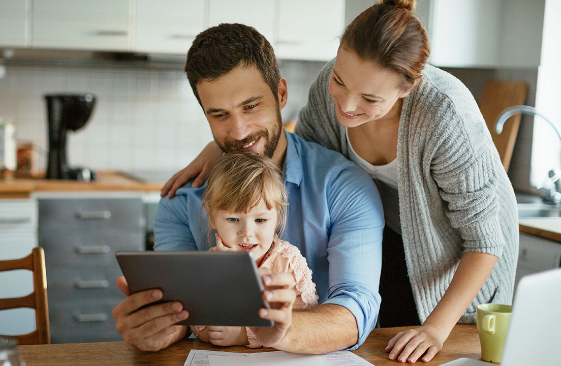 A family in the kitchen looks at a tablet together at the table