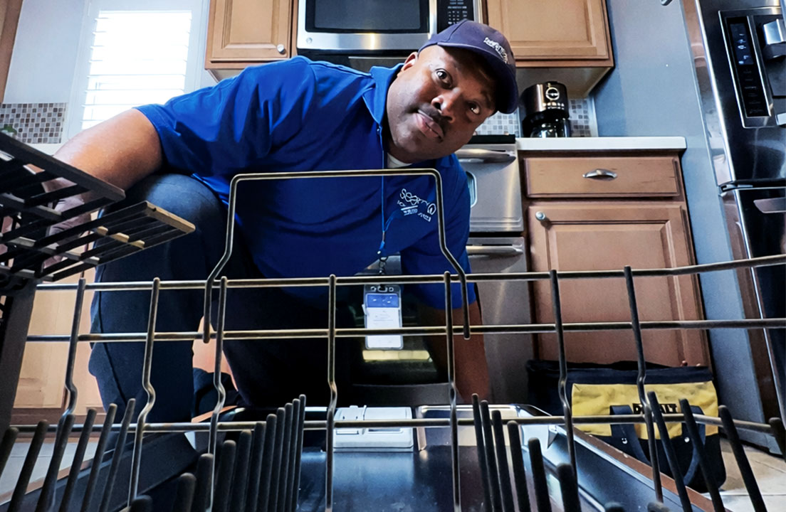 A Sears appliance technician leans into an open dishwasher to inspect the interior racks and components