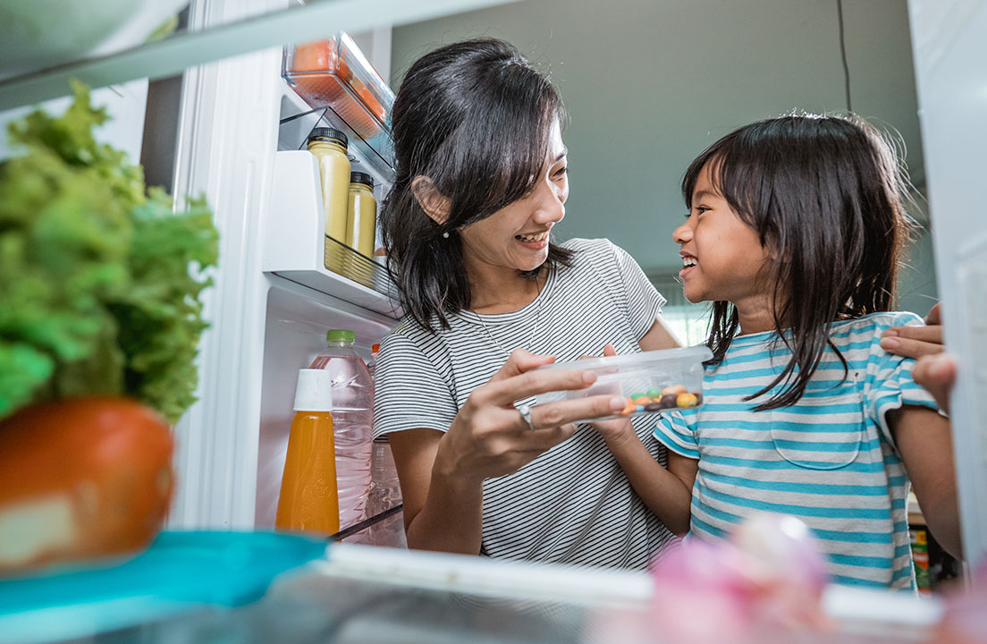 Adult and child smiling together while choosing food from an open refrigerator