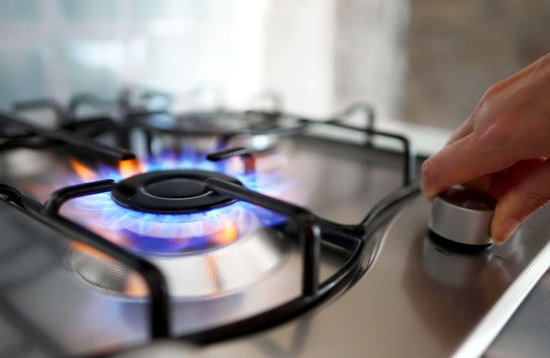 Close-up of a hand turning the knob on a lit gas stove burner