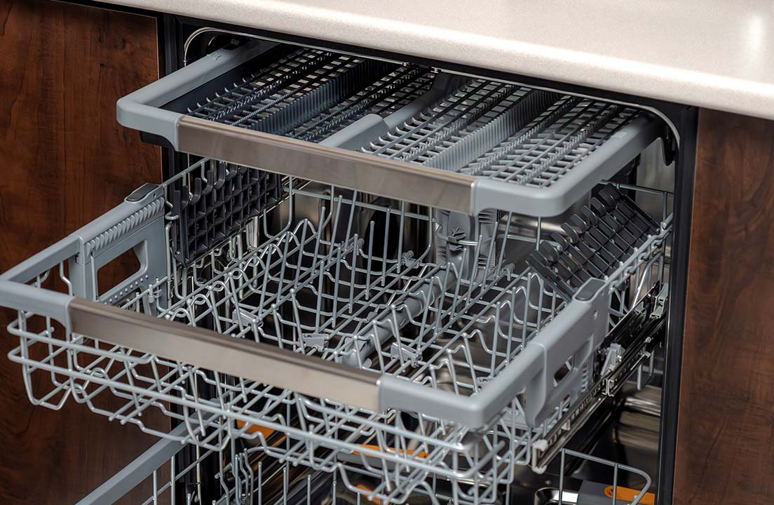 An open dishwasher shows its empty racks and utensil tray ready for loading