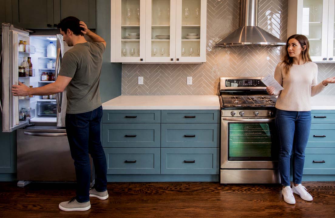 Homeowners look over paperwork while checking a refrigerator in a kitchen