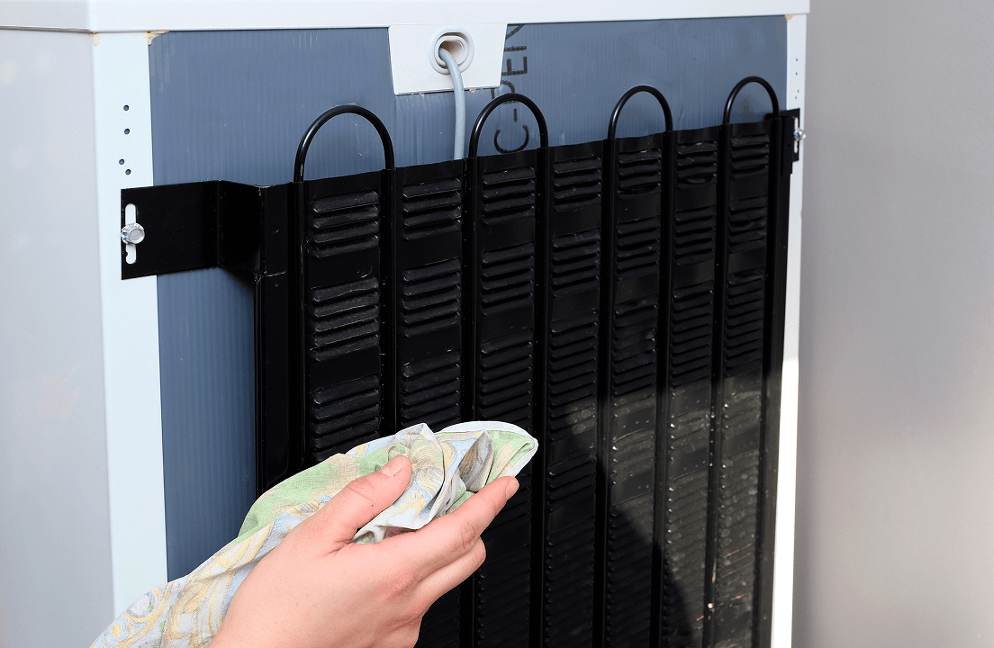 A person cleaning the back coils of a refrigerator