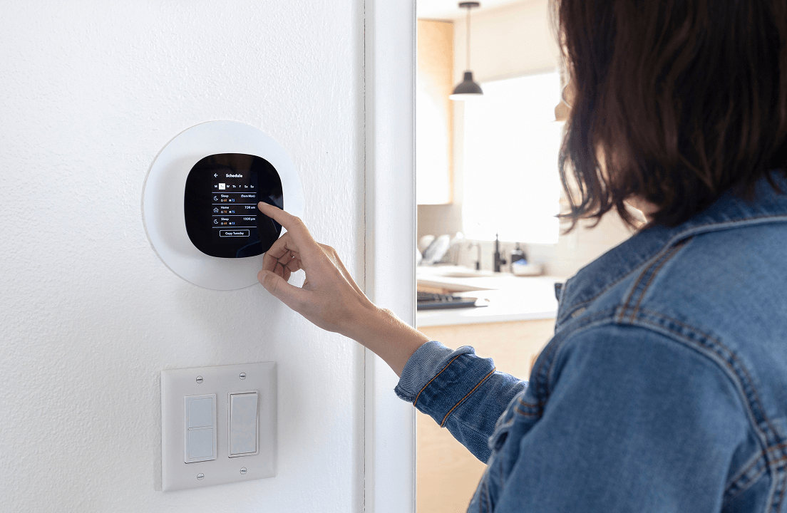 A woman adjusting a smart theromstat in a kitchen