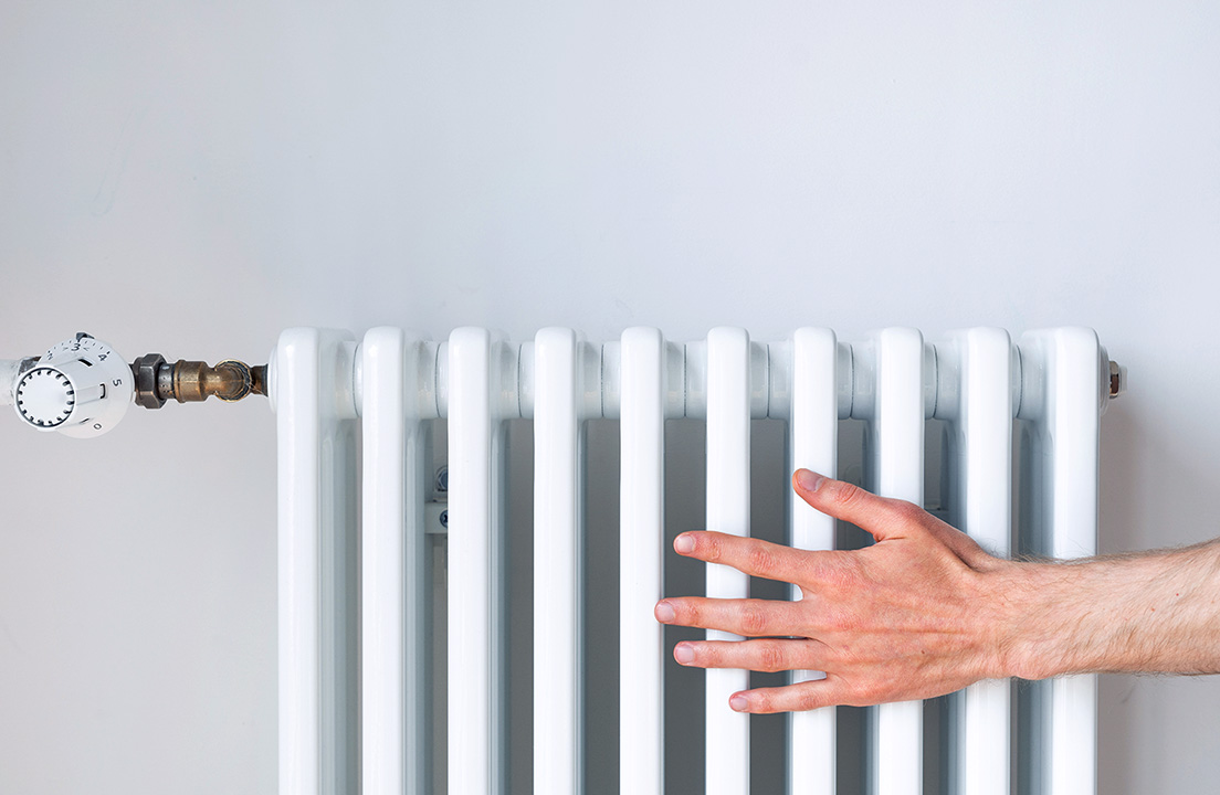 A person’s hand resting on a white home radiator to check the heat
