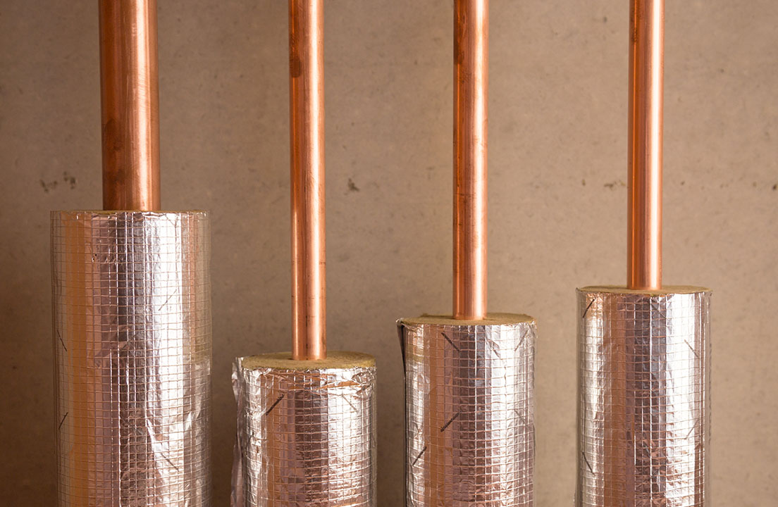 Close up of copper pipes wrapped with shiny insulation to protect them from heat loss and freezing