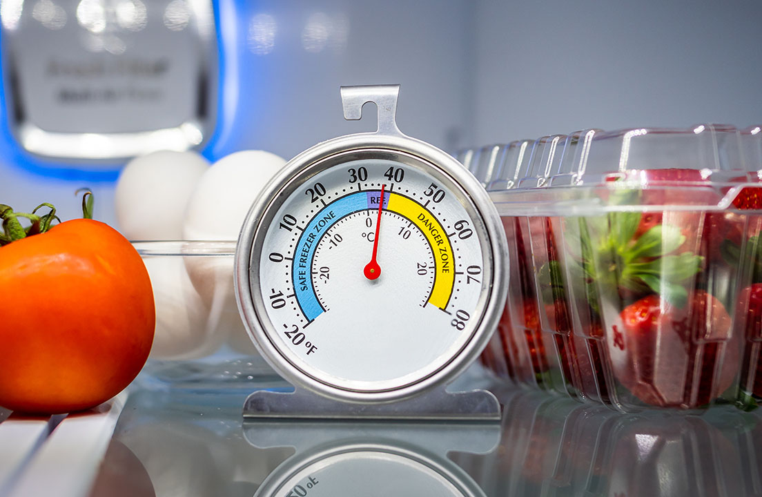 A refrigerator thermometer sits near 40°F on a shelf next to eggs and containers of fresh food