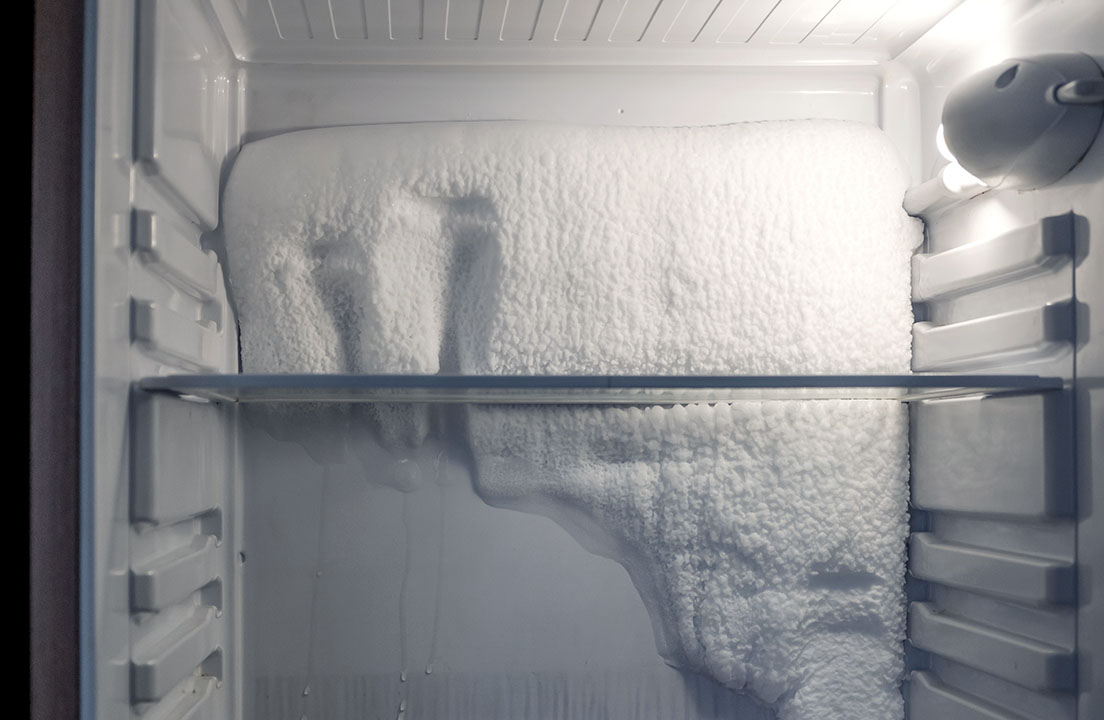 Heavy ice buildup blankets the back wall of a freezer compartment beneath a glass shelf