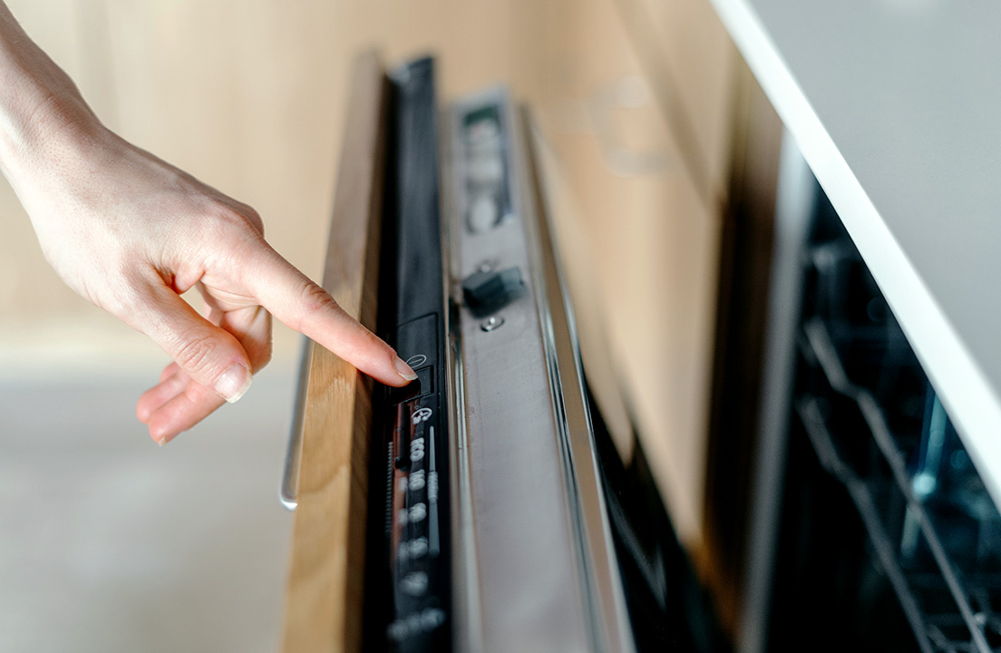 A person presses a setting on the control panel of a built-in dishwasher