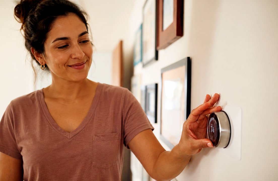 A woman adjusts a thermostat to help keep her home comfortable