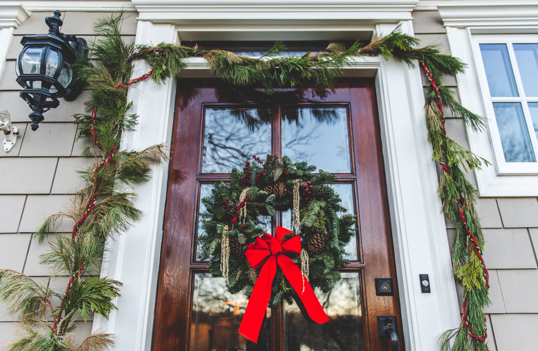 Front door decorated with a holiday wreath and garland, featuring a bright red bow to welcome guests