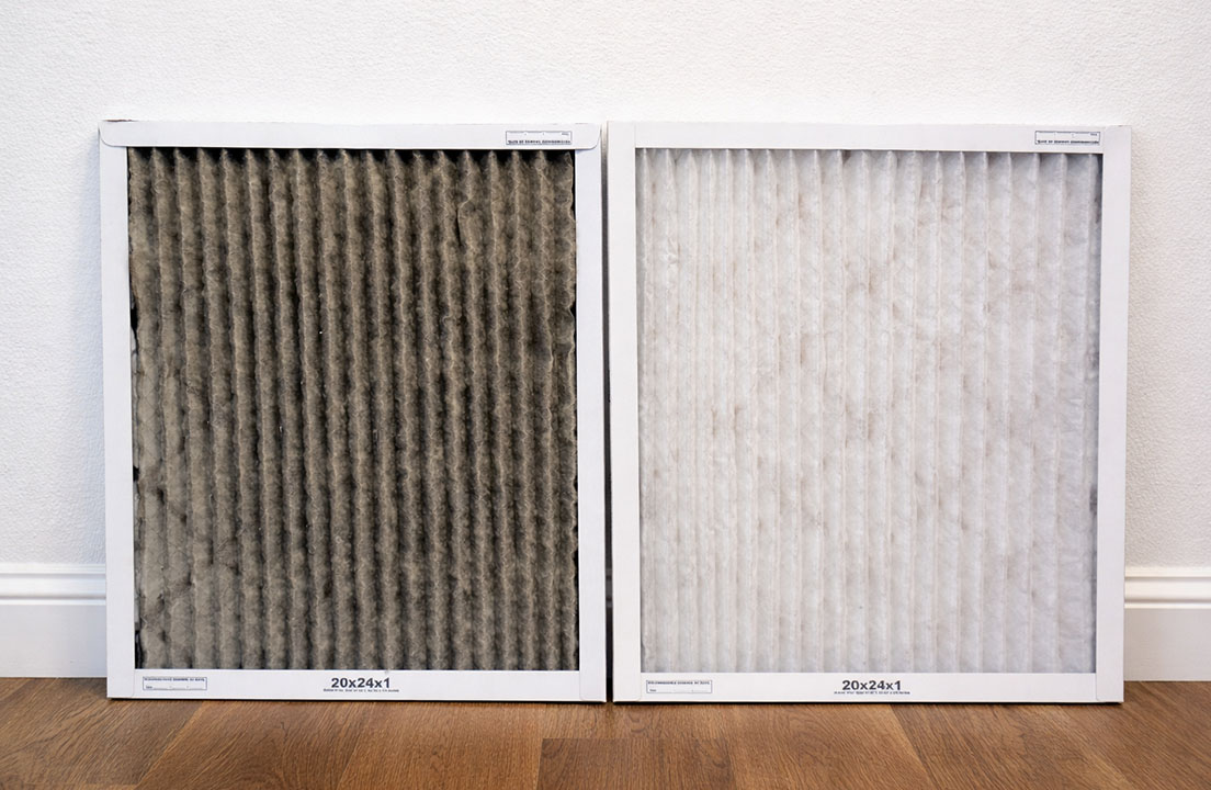 A dirty air filter stands next to a clean replacement filter on a hardwood floor