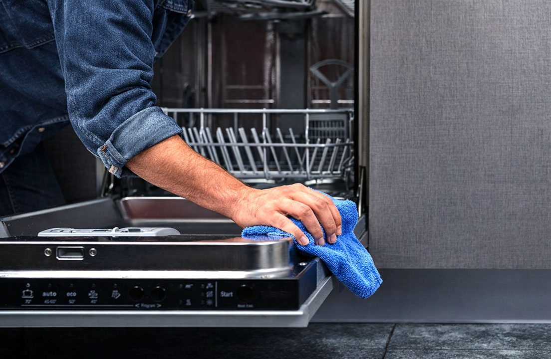 Person wipes the edge of an open dishwasher door with a blue microfiber cloth