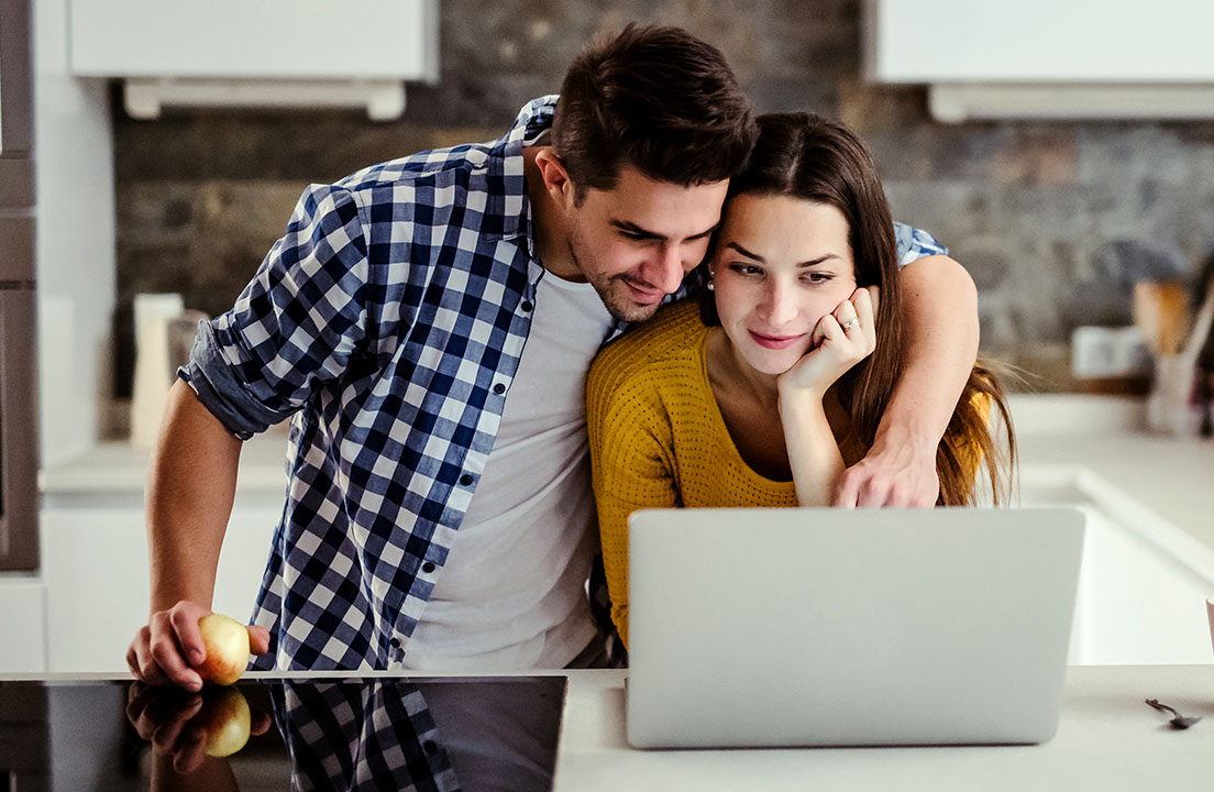 A couple reviews information on a laptop together at a kitchen counter