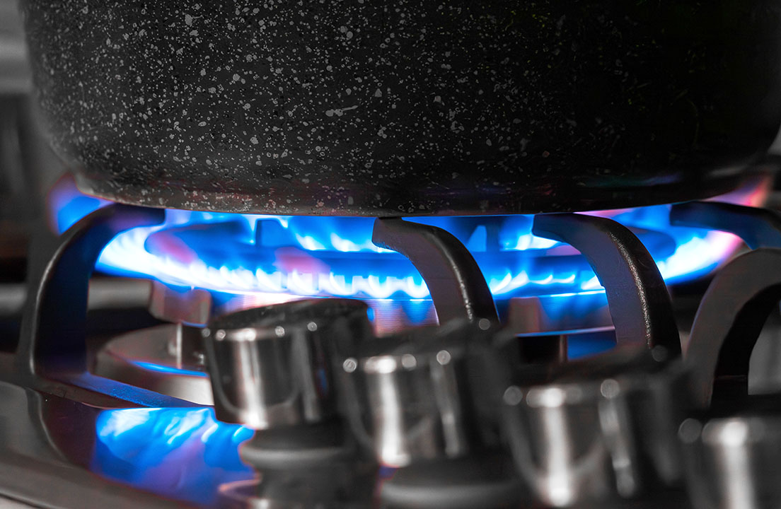 Close-up of a pot heating on a gas stove with bright blue flames visible beneath the burner grate