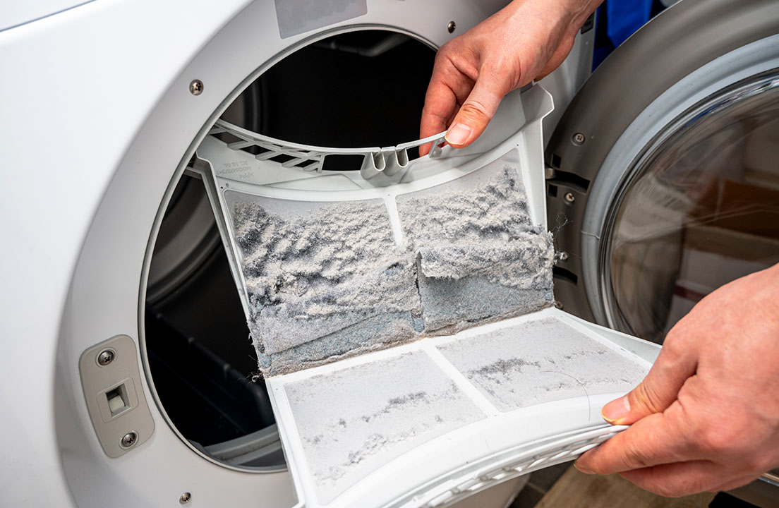 A person cleaning a lint trap within a dryer and while showing mounds of lint on top