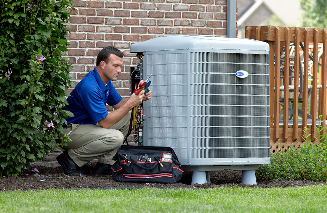Technician servicing an outdoor air conditioning unit beside a brick home