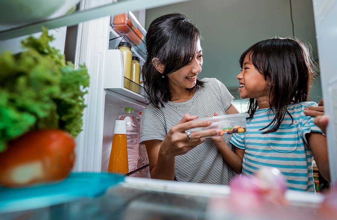 Parent and child smiling while choosing food from the refrigerator