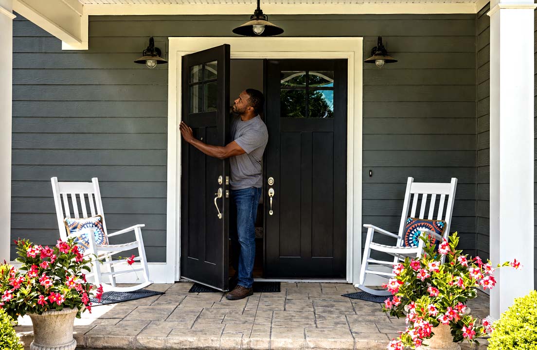 A man opens the front door and checks the weather-sealing around the frame