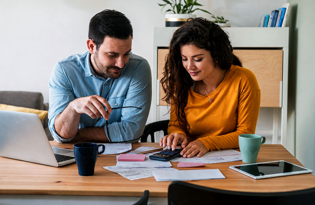 A couple reviews bills and home warranty paperwork together at a kitchen table