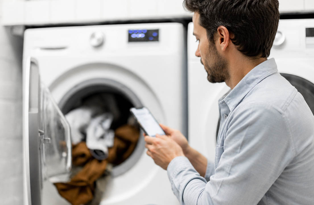 Man checks his phone beside an open dryer containing a load of laundry