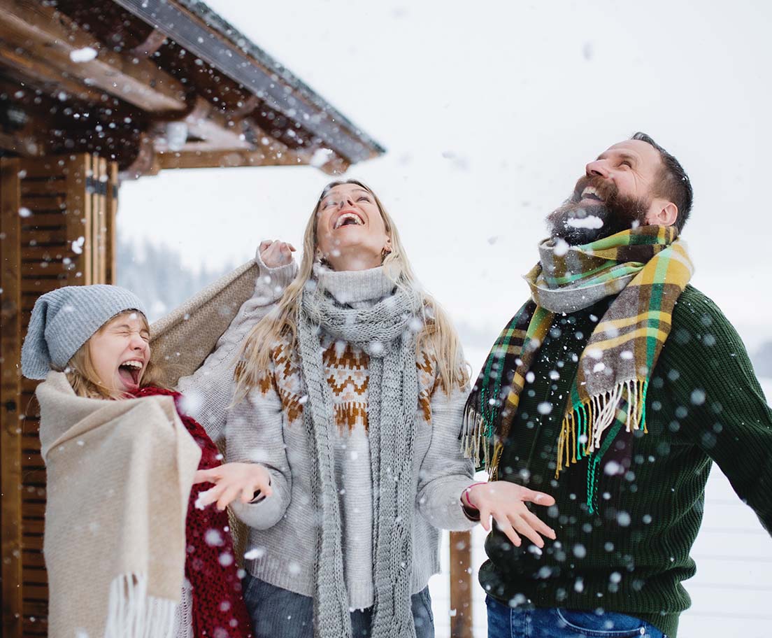 A family bundled in winter clothing laughs joyfully as snow falls around them