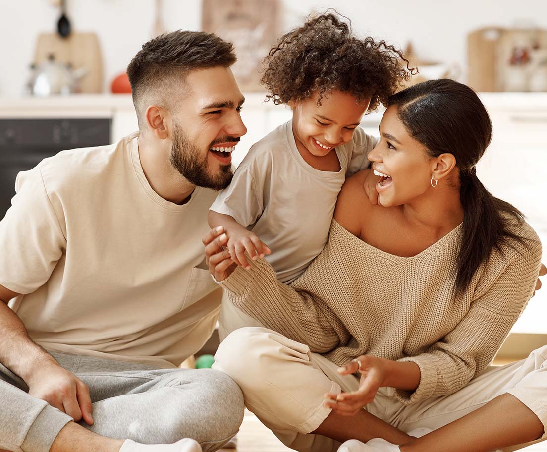 A couple laughs with their child while sitting together at home
