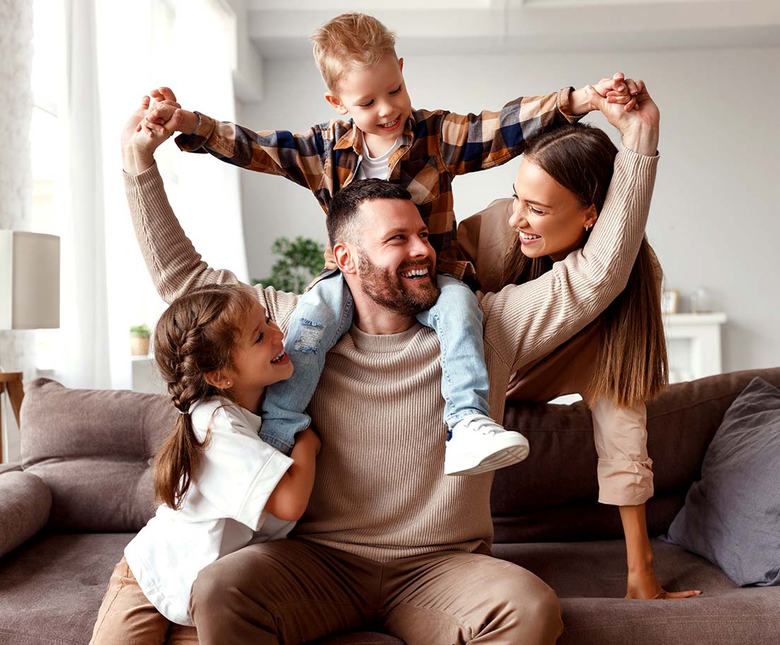 A smiling family relaxes on a couch while the kids play, enjoying a comfortable living room