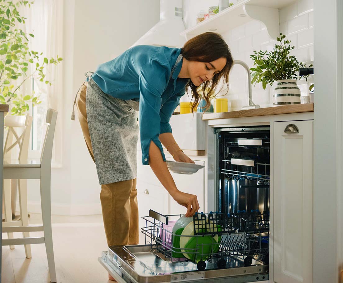 Woman loading dishes into an open dishwasher in a bright kitchen