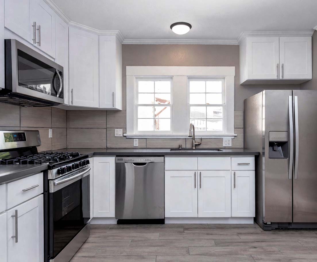 Bright modern kitchen with white cabinets and stainless steel appliances including a stove, microwave, dishwasher, and refrigerator