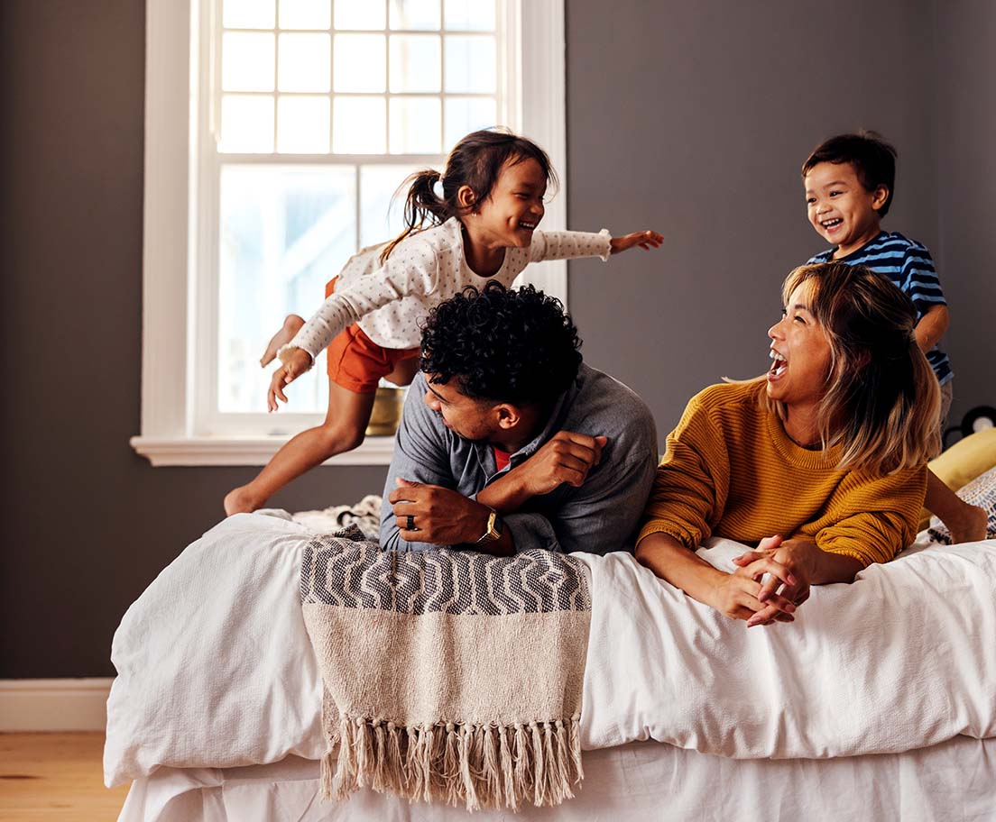 A family laughs and plays together on a bed in a bright bedroom