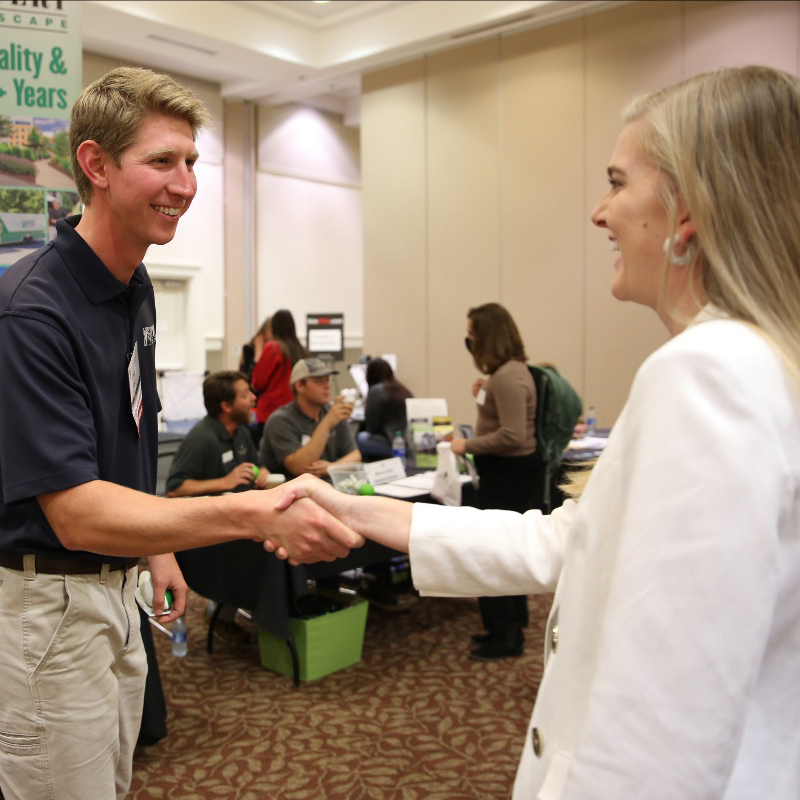 A man and a female student shake hands at a career fair.