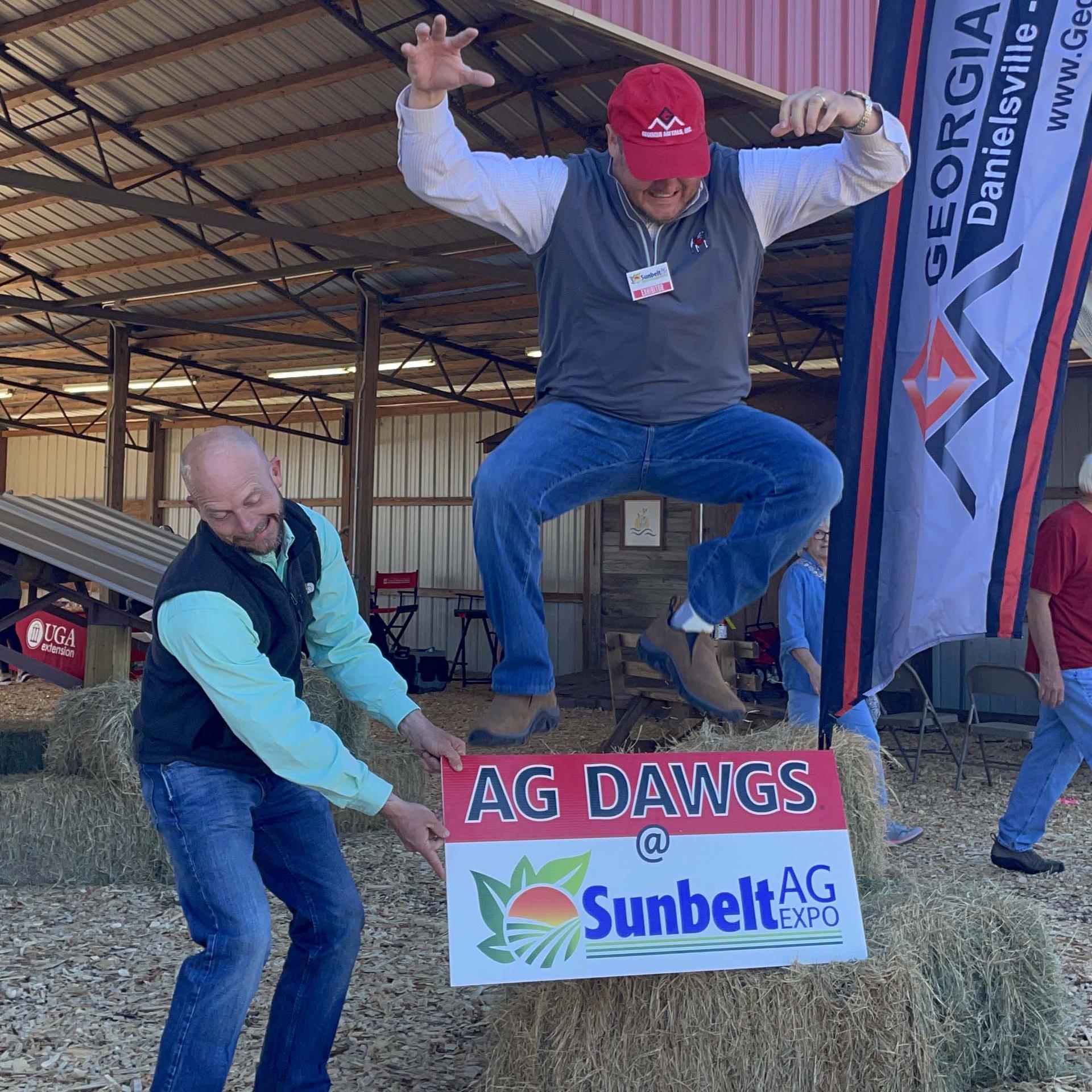 Tripp Strickland jumping over the Ag Dawgs at Sunbelt Ag Expo sign. Held by Byron Lee.