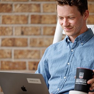 an OMBA student works on a class on his laptop on his front porch